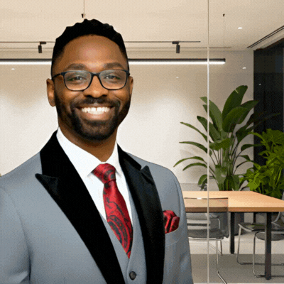 Man in gray suit and red tie, smiling with glasses in office setting. Angelo Austin.