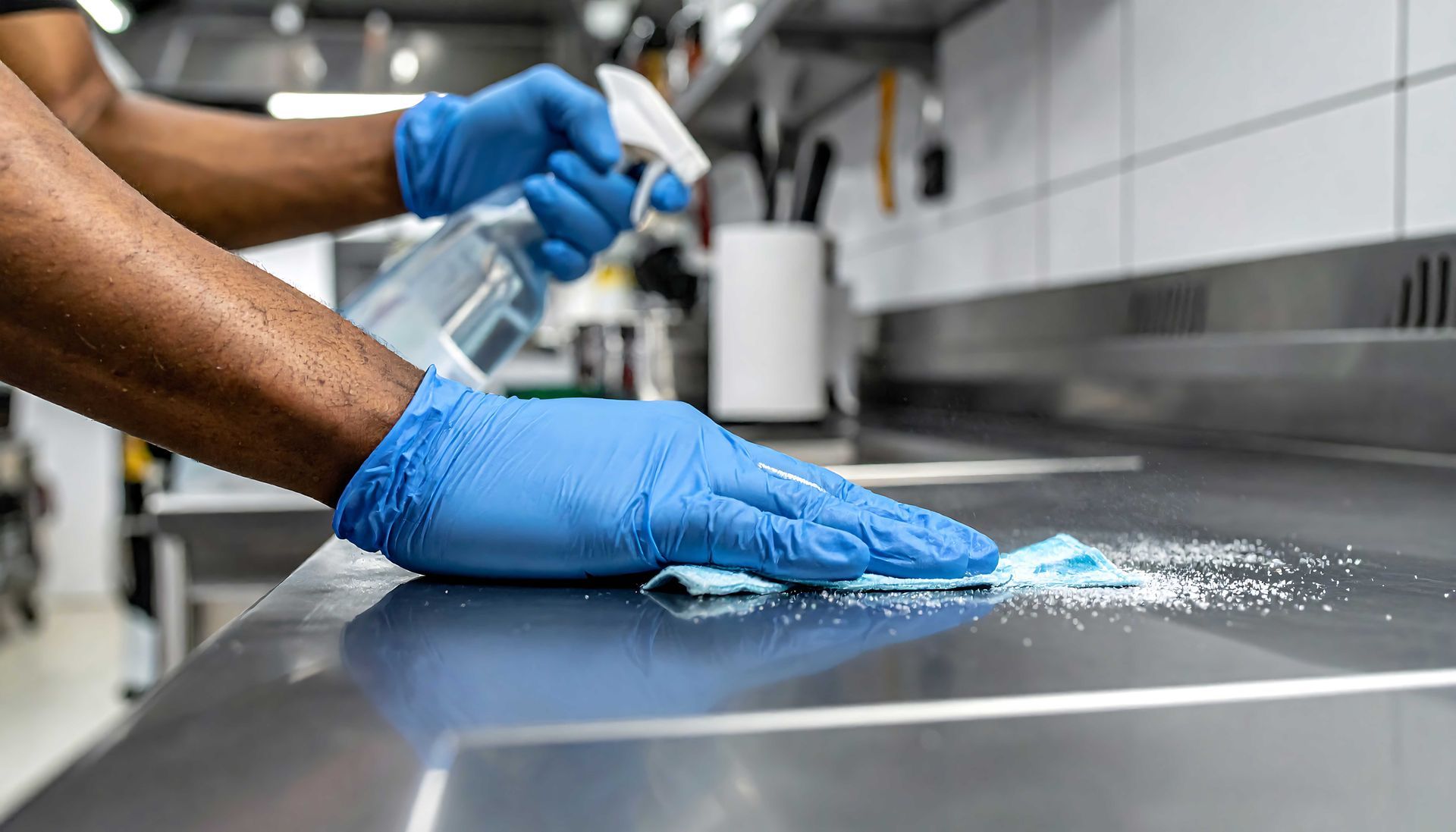 Blue-gloved hands cleaning a stainless steel counter in a commercial kitchen Blue-gloved hands cleaning a stainless steel counter in a commercial kitchen