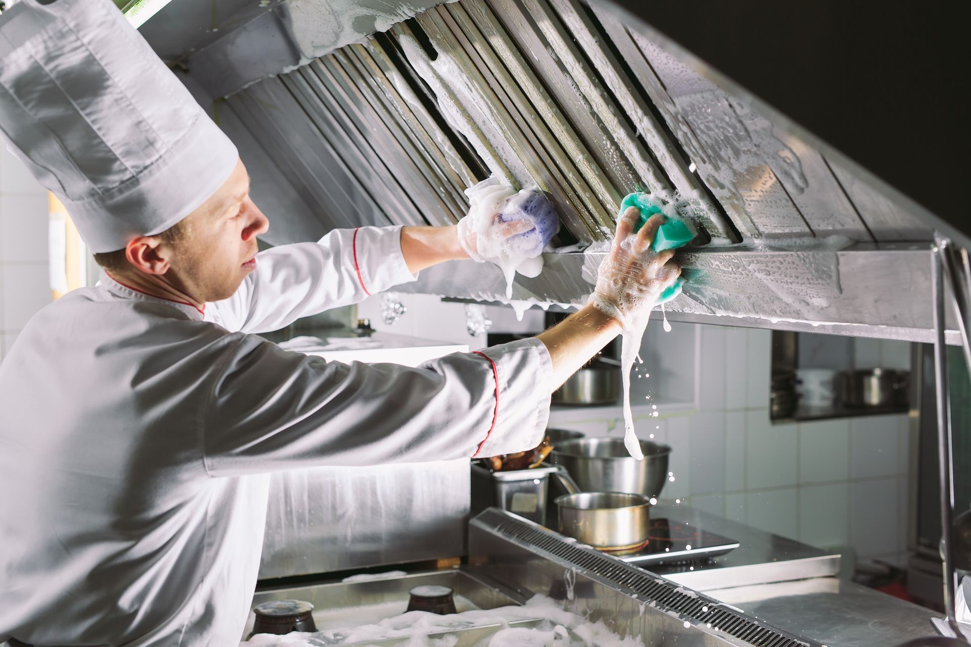 A chef is cleaning a kitchen hood.