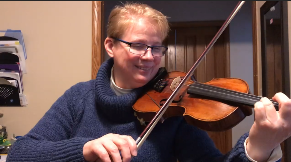 A woman in a blue sweater is playing a violin