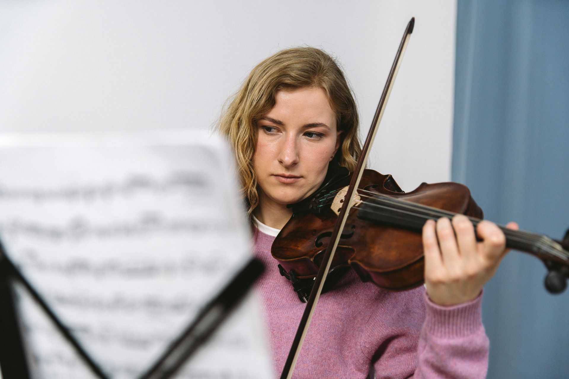 A woman in a pink sweater is playing a violin.