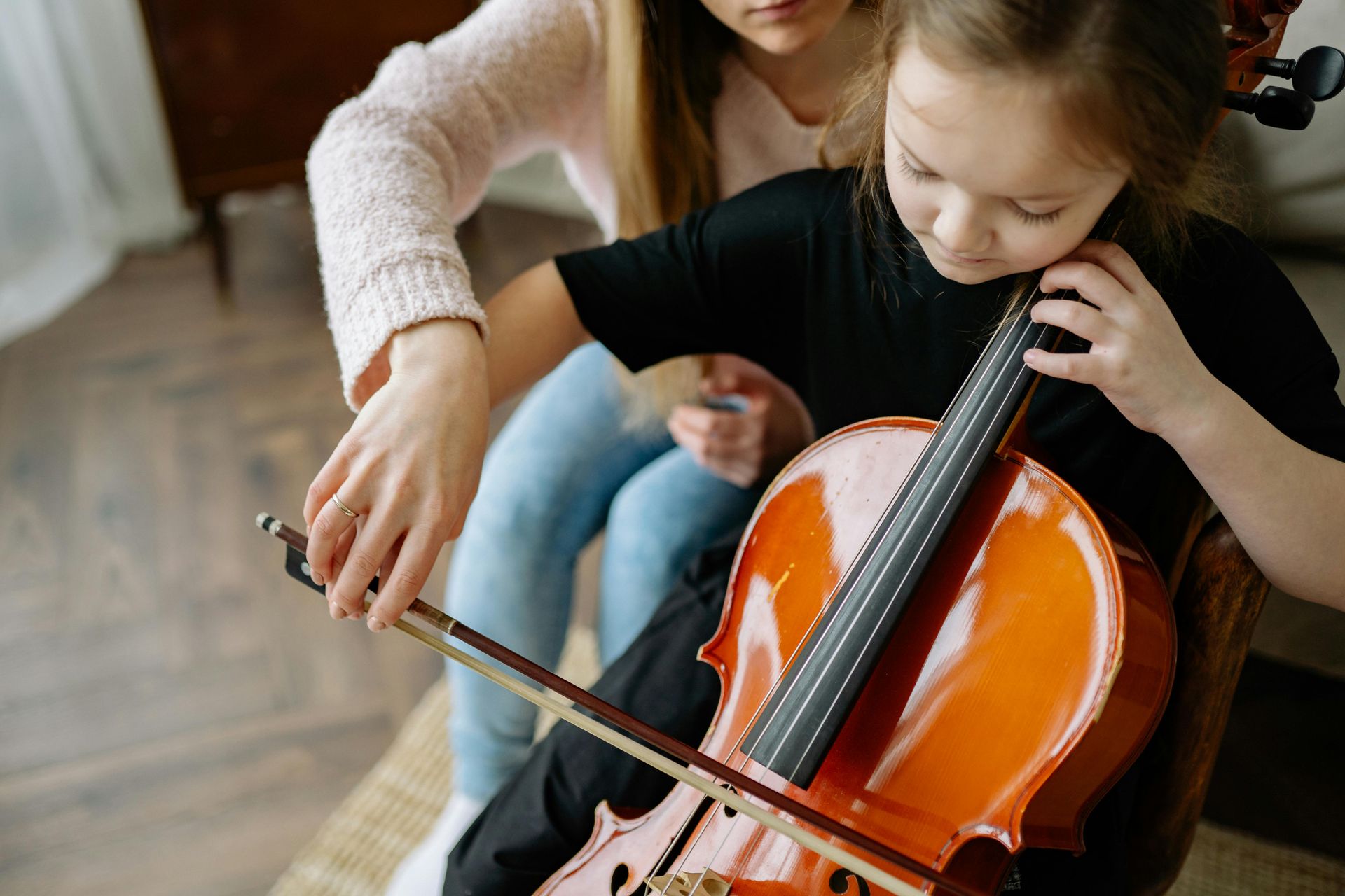 A woman is helping a little girl play a cello.