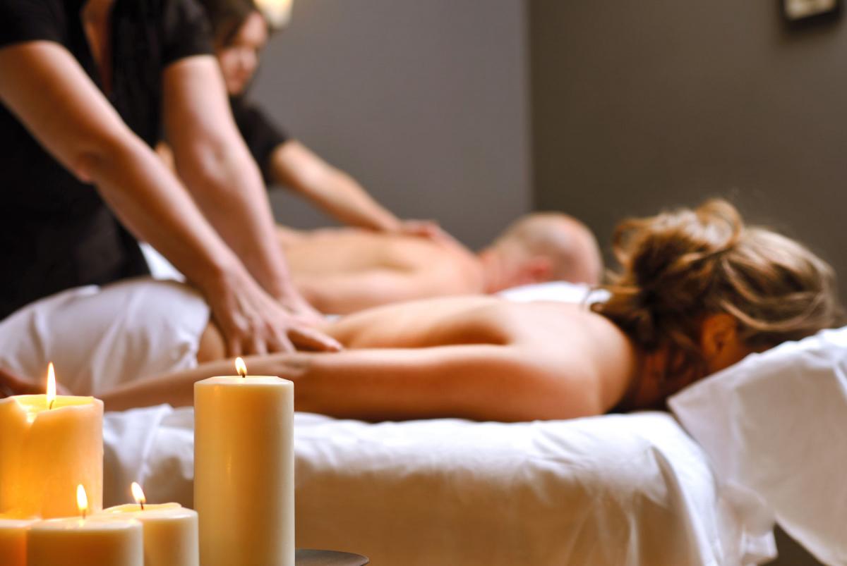 Two people receiving massages in a spa, with lit candles and soft lighting.