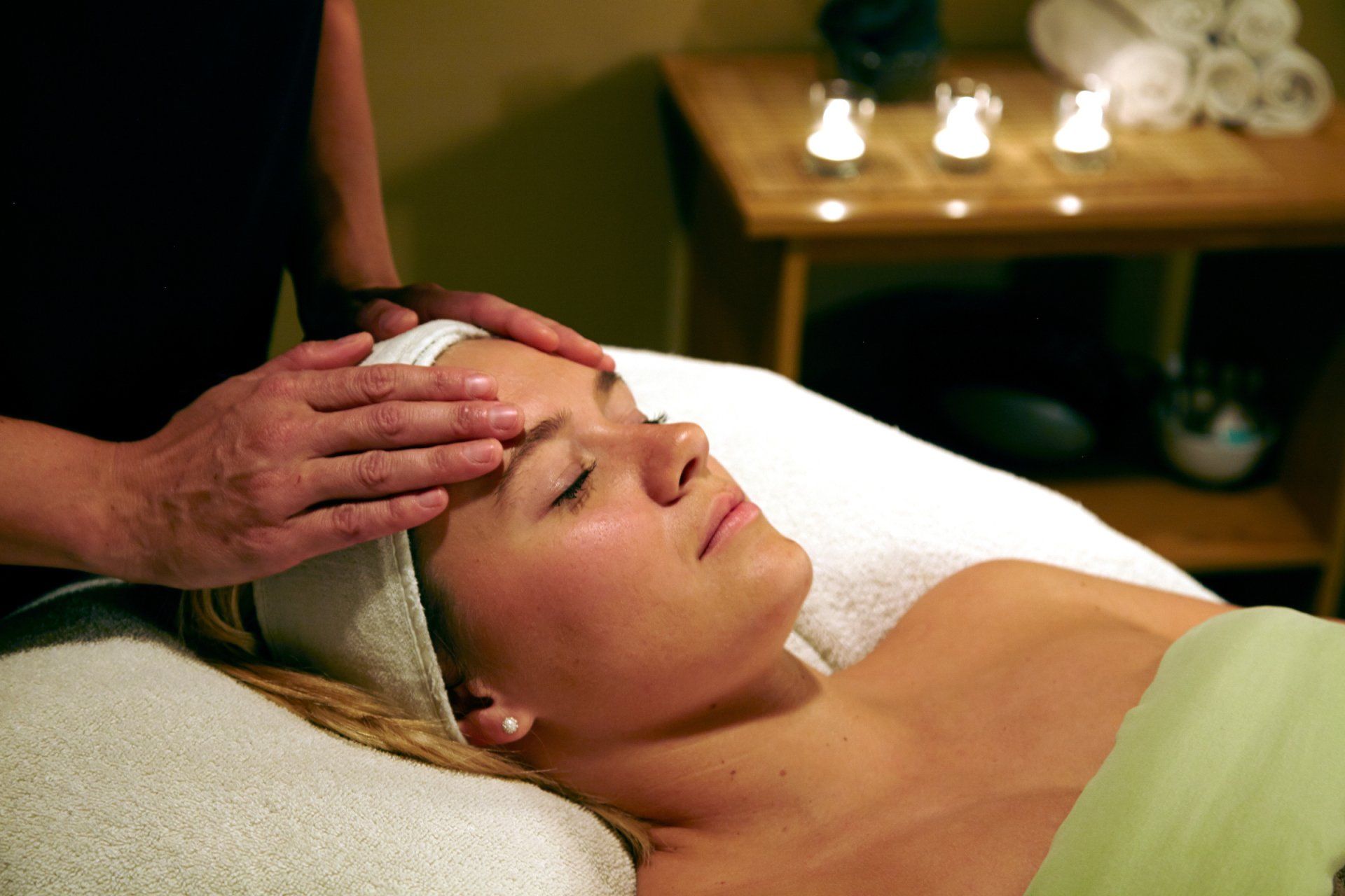 Woman receiving a facial massage at a spa; hands on forehead, eyes closed.