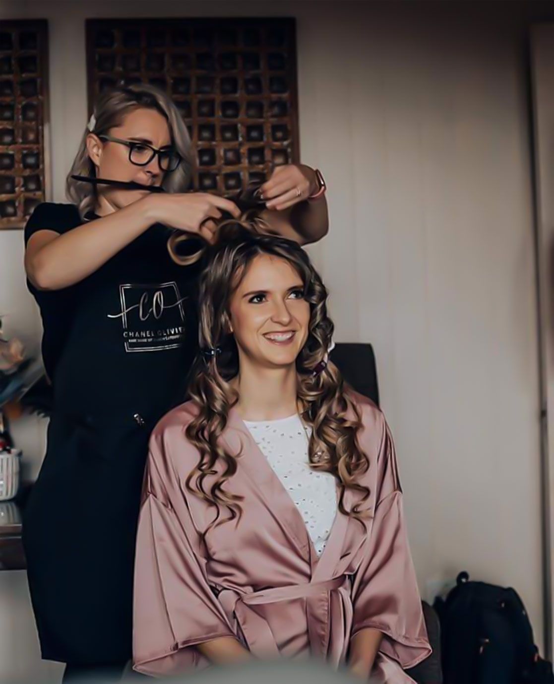Woman getting her hair styled. A hairstylist in a black apron is curling the woman's hair.