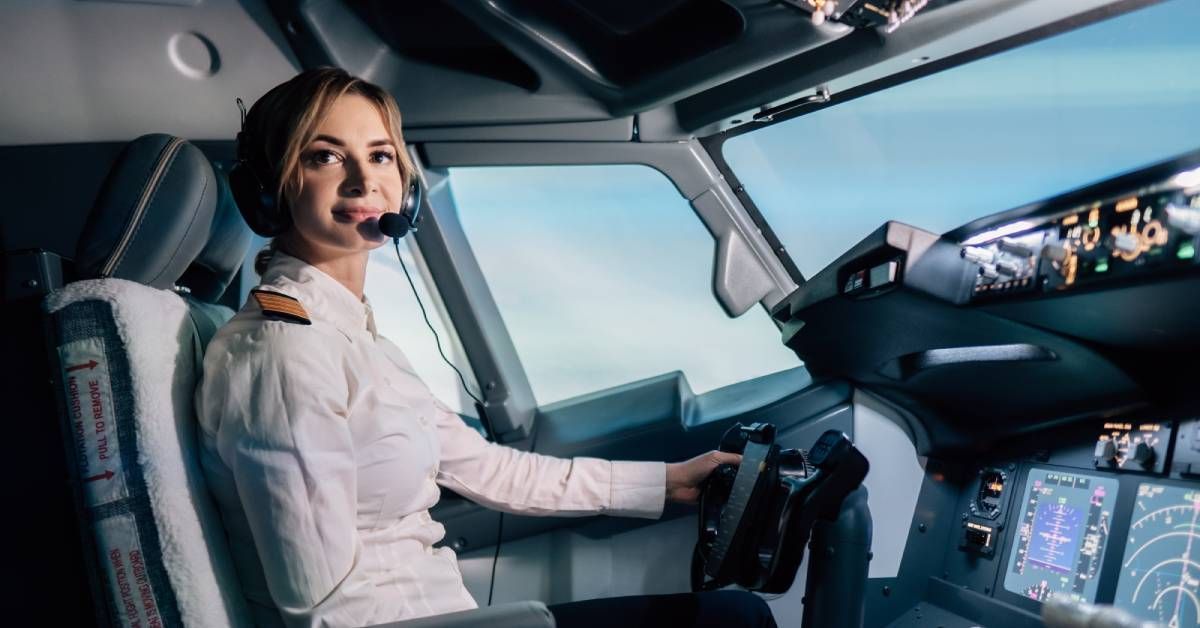 A commercial airline pilot looks around the cockpit with a happy look on their face as the plane flies through clouds.