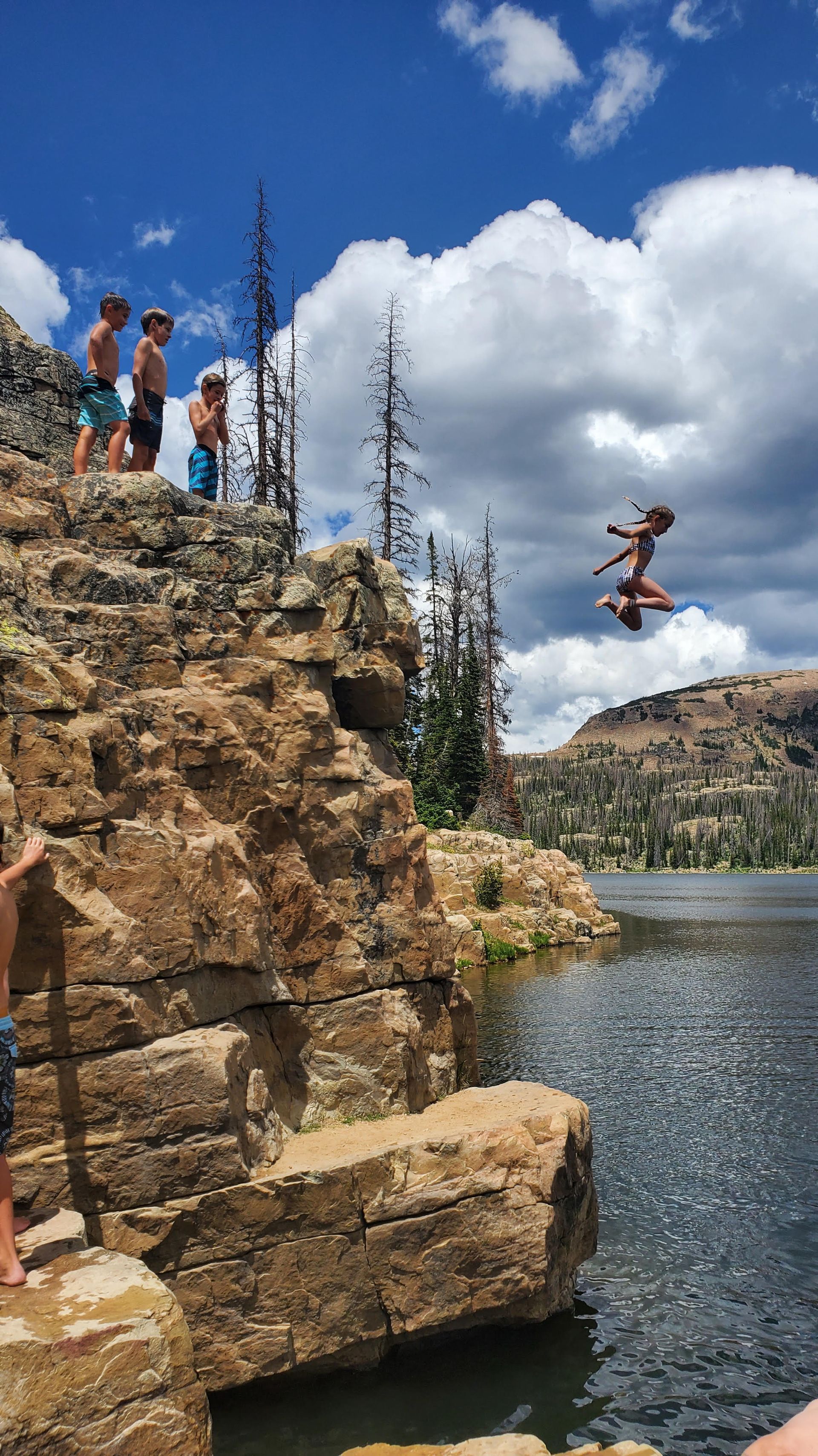 People cliff jumping into a lake on a sunny day.