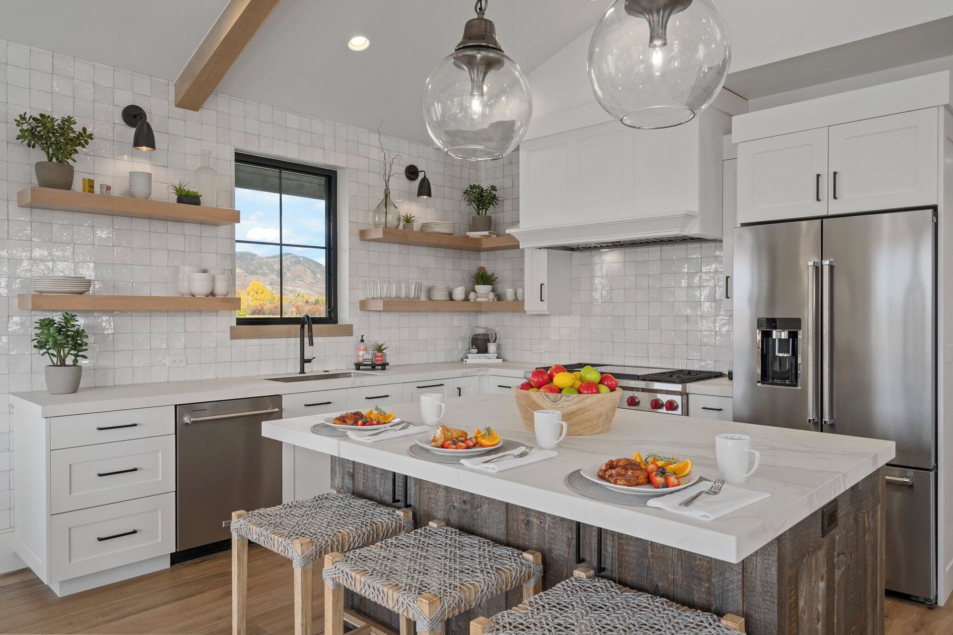 Bright kitchen with white cabinets, island, and open shelving.  Features a stainless steel refrigerator and window.