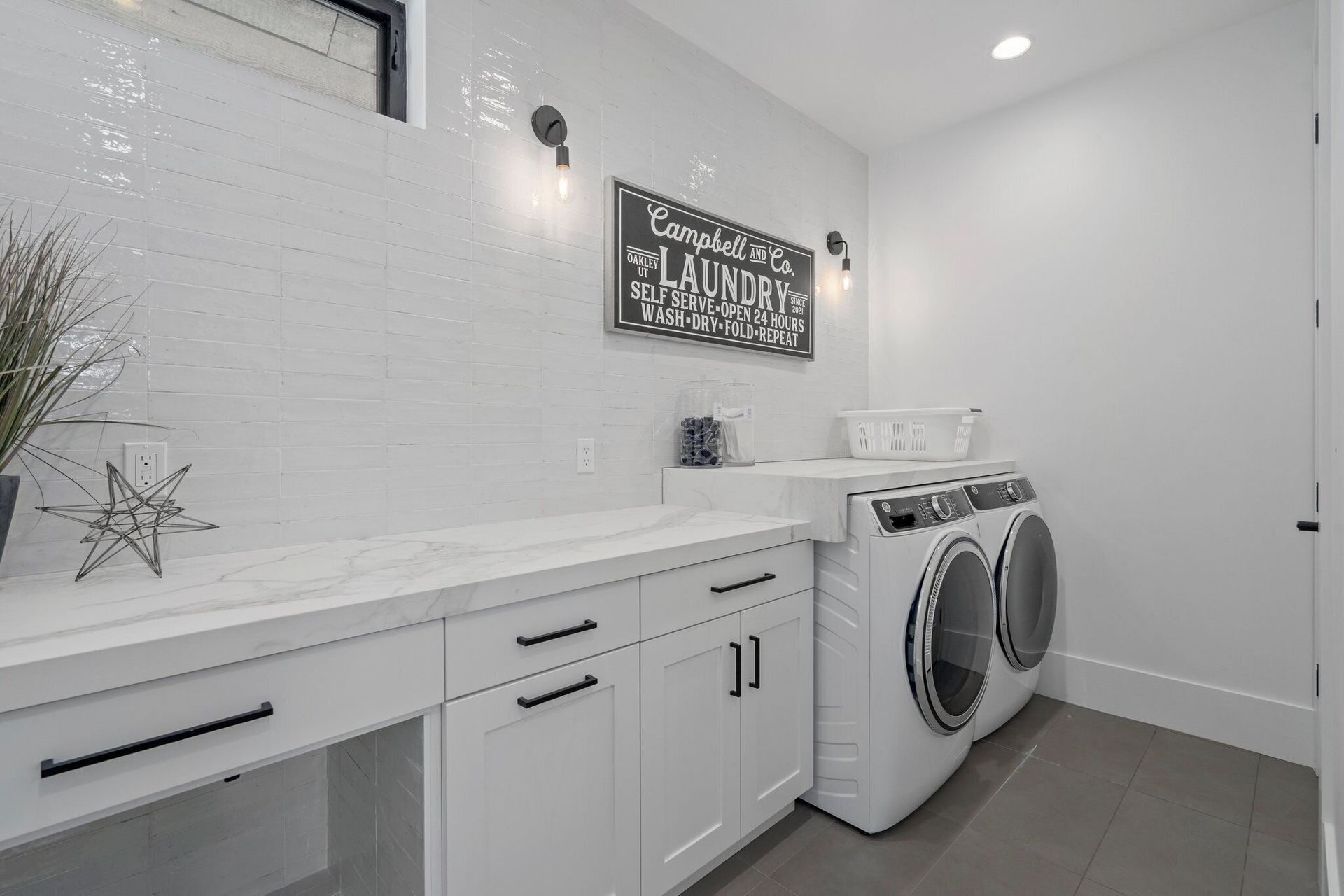Modern white laundry room with appliances, cabinets, and decor.