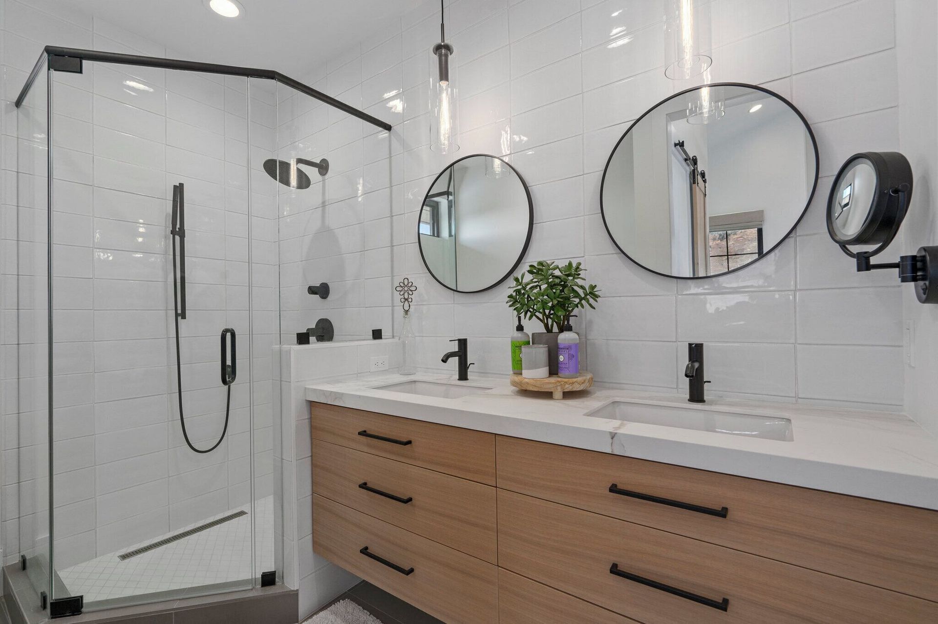 Modern bathroom with a glass shower, double vanity, and round mirrors.