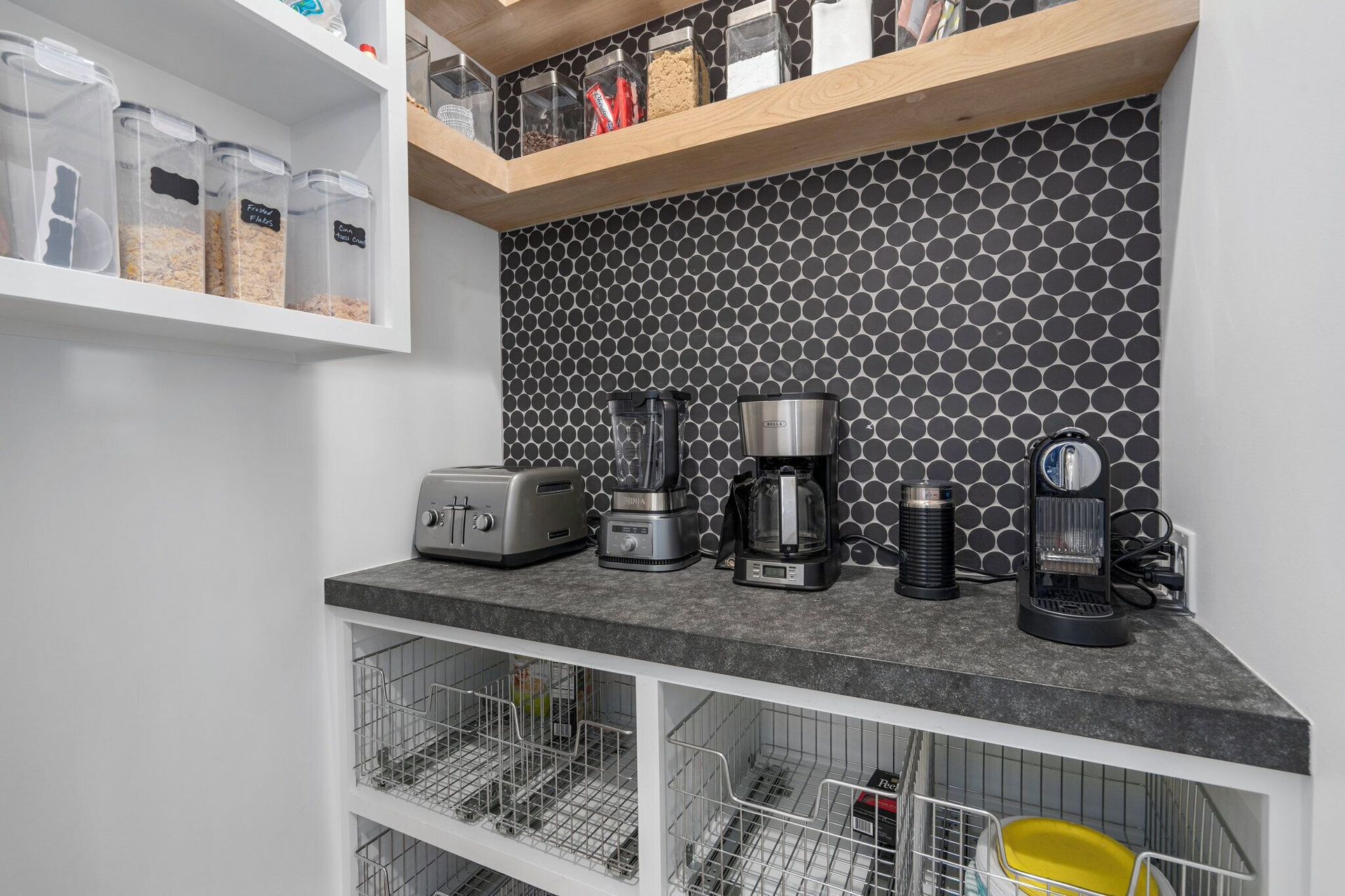 A kitchen pantry with a countertop, appliances, tile backsplash, and storage shelves.