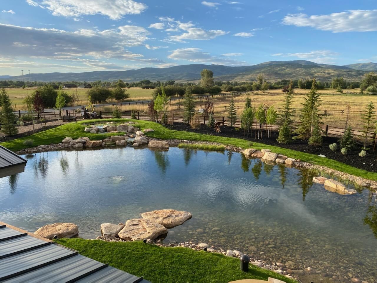 Pond reflecting a blue sky and surrounding landscape with mountains in the distance.