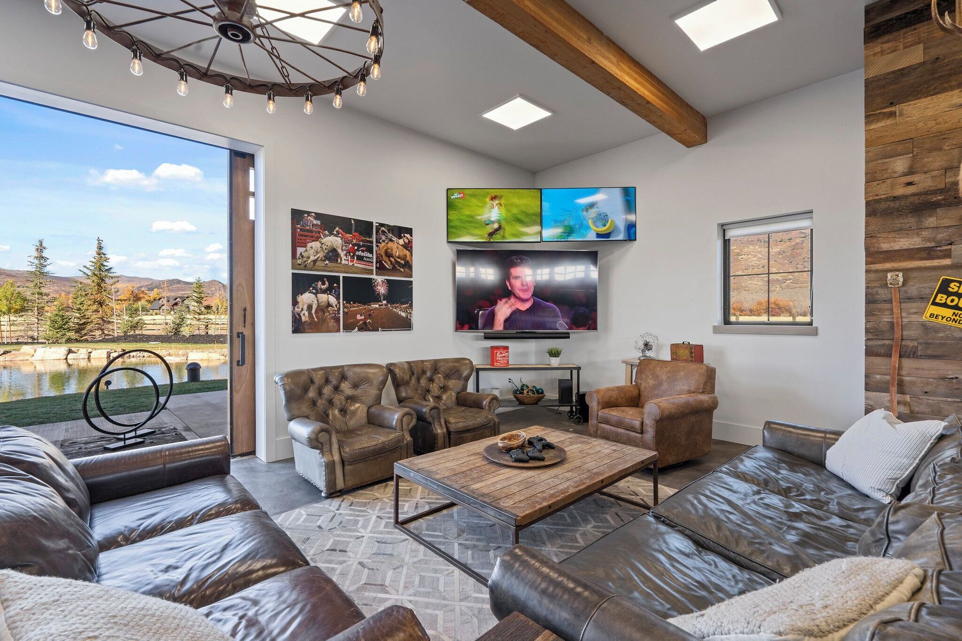 Living room with leather furniture, multiple TVs, and a view of a lake.