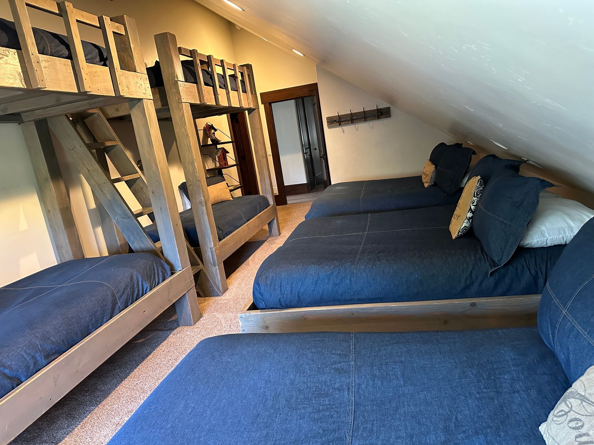 A room with bunk beds and three twin beds; all with blue bedding, located in a loft.