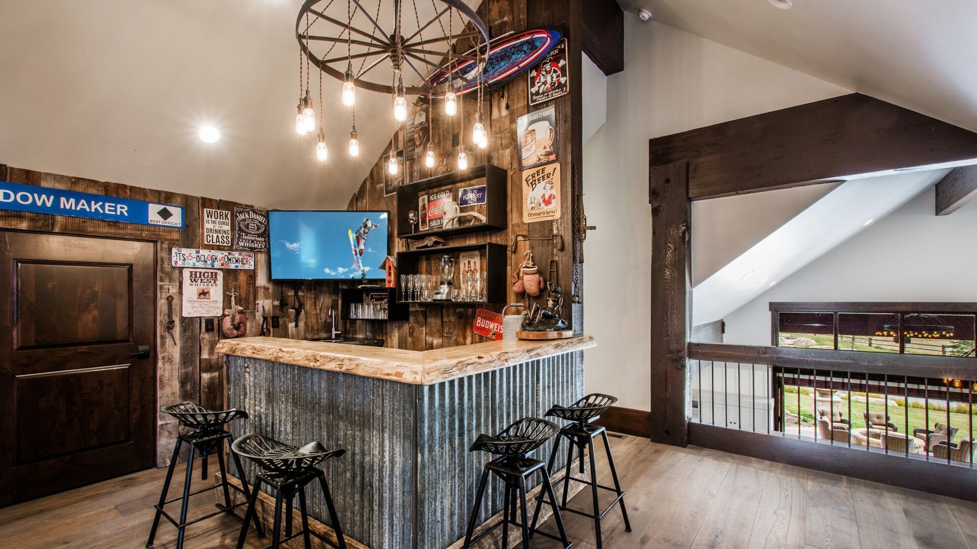 Rustic home bar with corrugated metal, wood, TV, and wagon wheel light fixture.