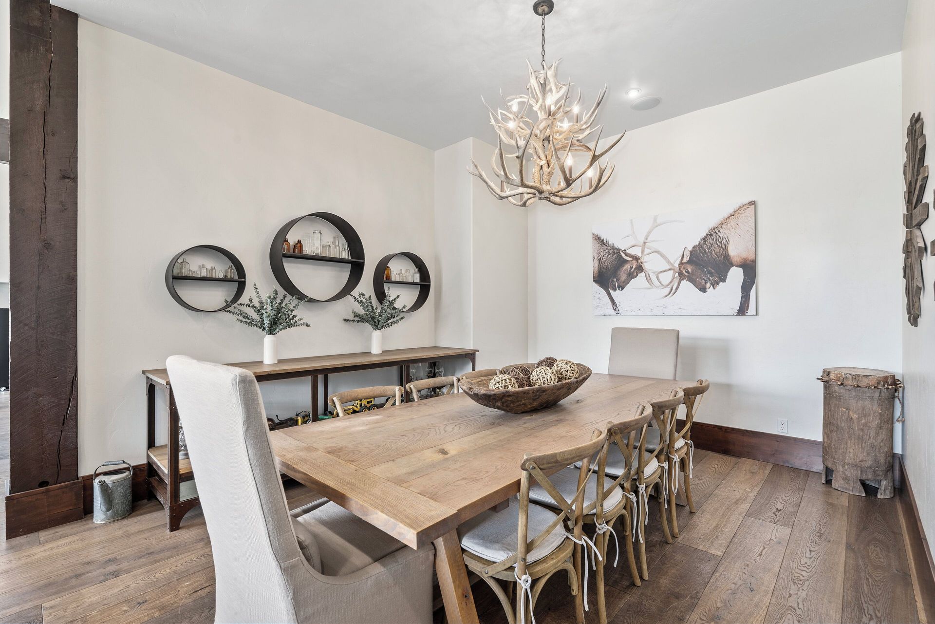 Dining room with wooden table, chairs, and decorative elements, including antler chandelier and artwork.