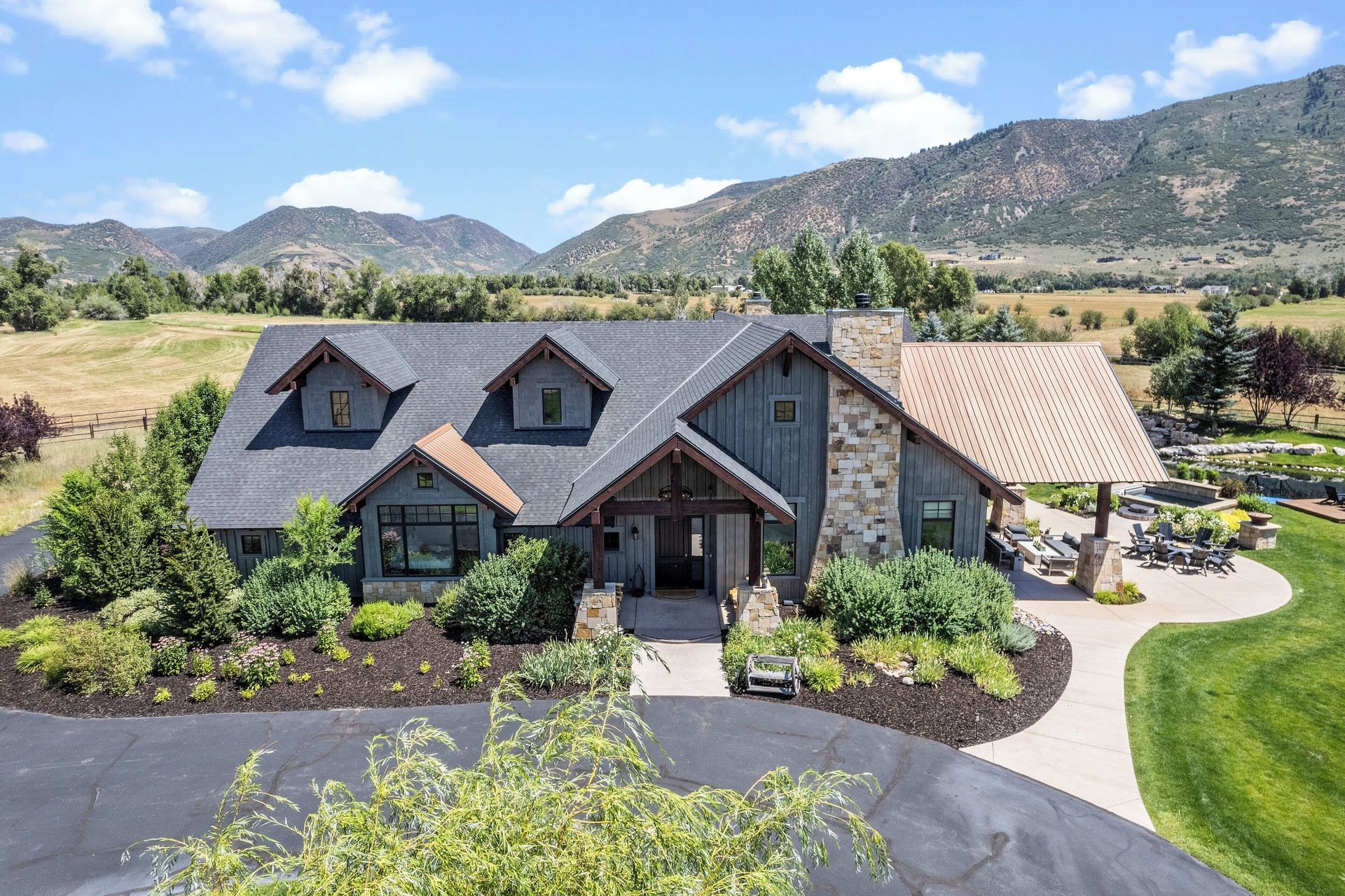 Large house with stone and blue siding, green lawn, mountain backdrop.