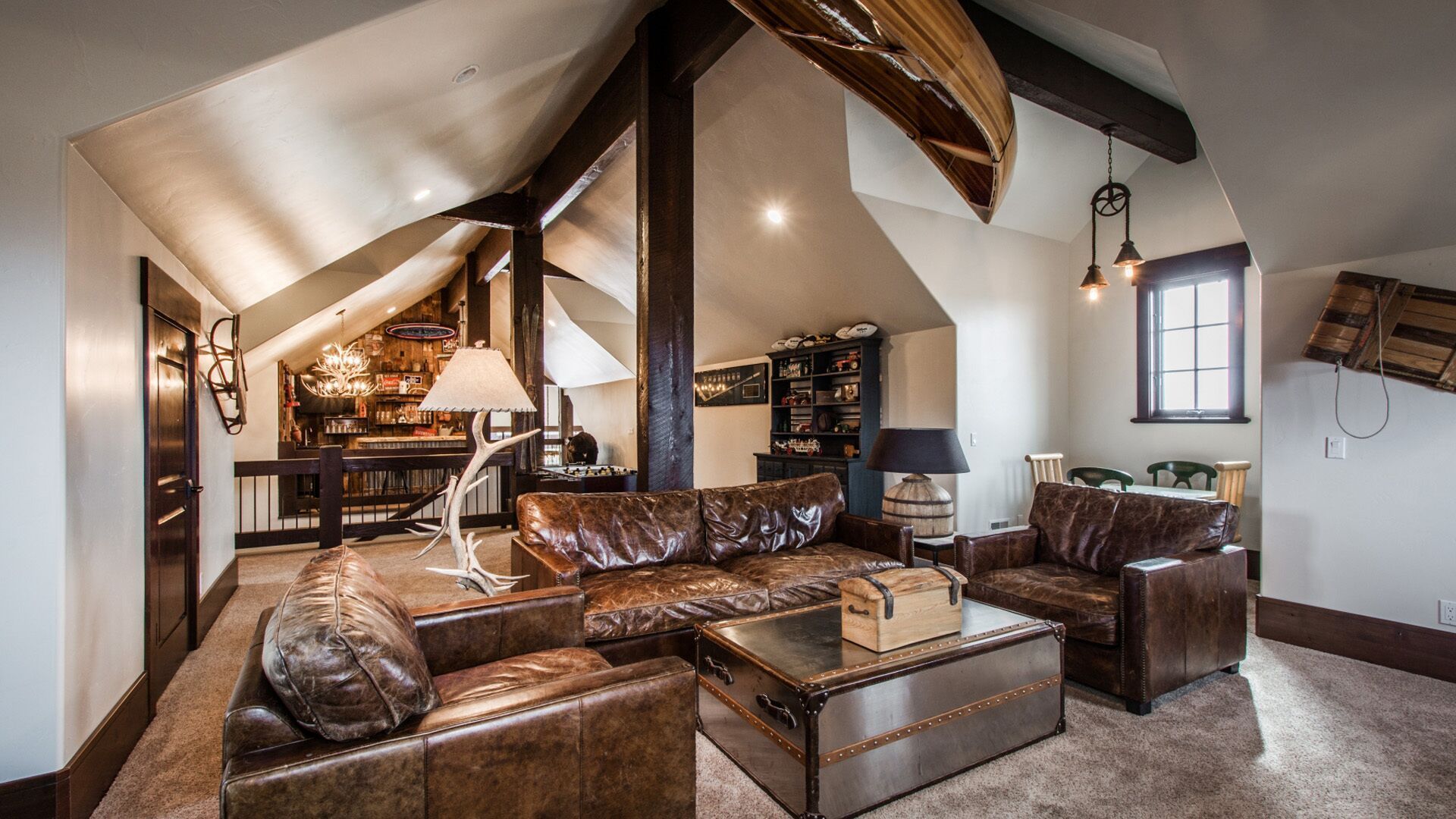 Loft living room with brown leather seating, a wooden canoe, and a desk in a rustic setting.
