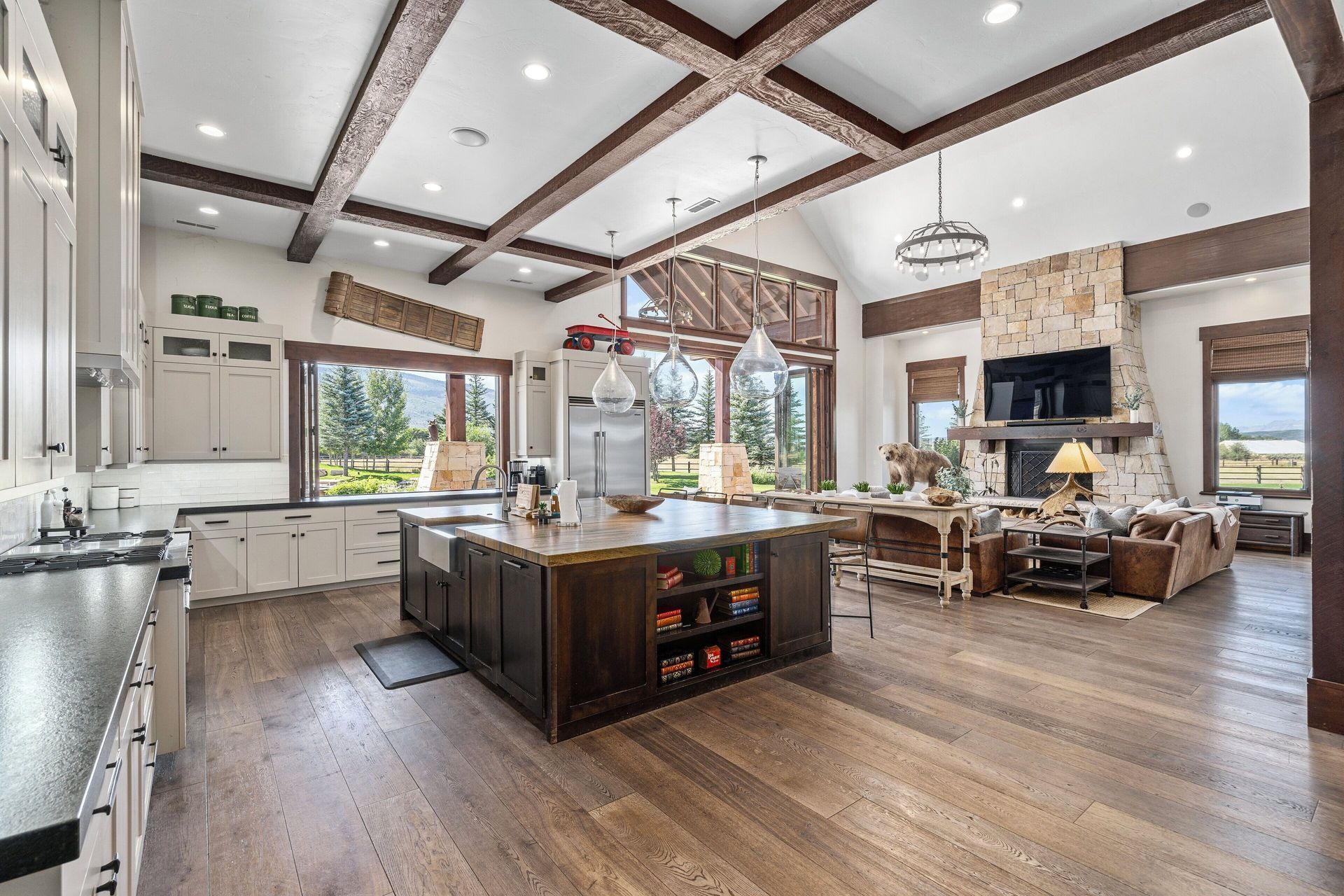 Open-concept kitchen with dark wood island, exposed beams, and a fireplace in a spacious, light-filled room.
