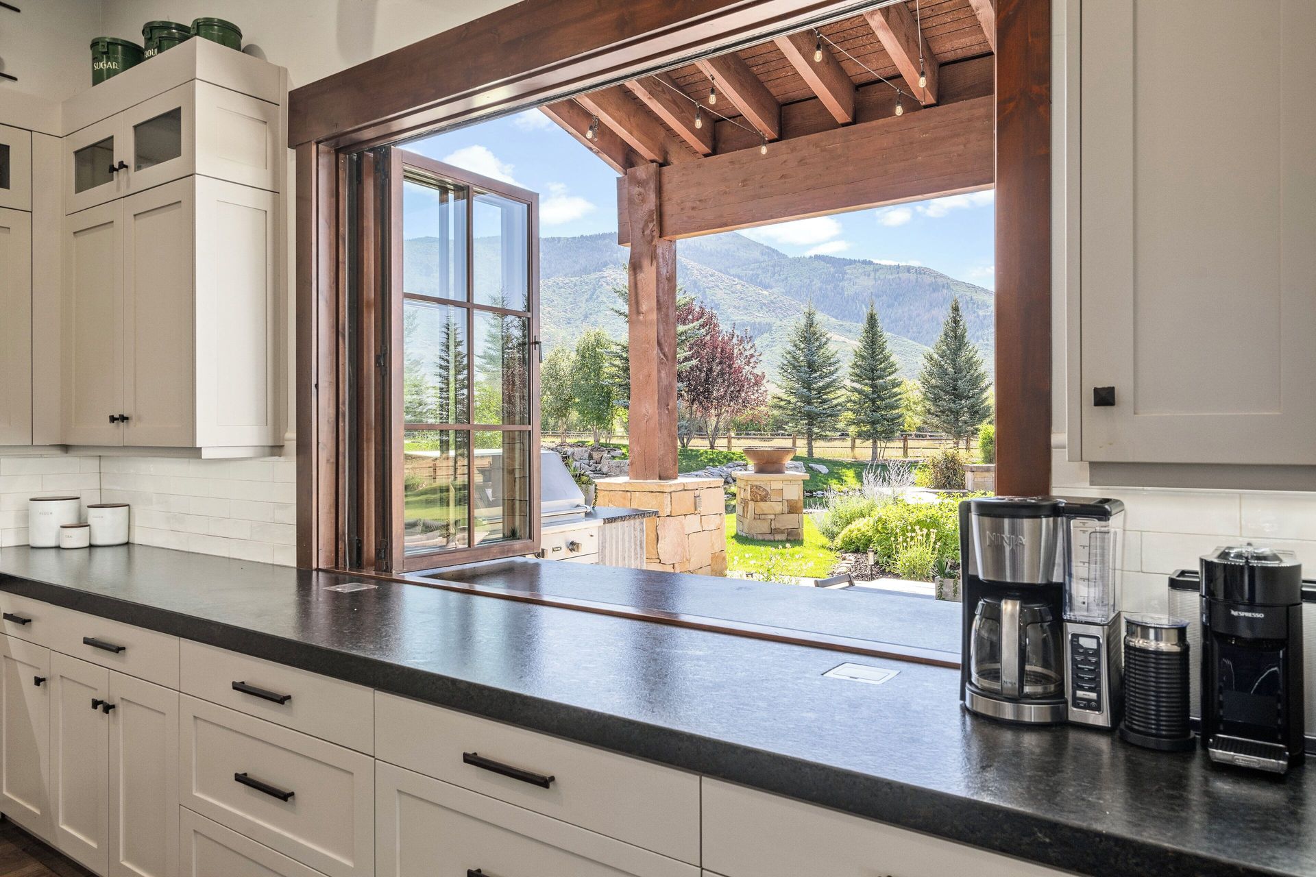 Kitchen counter with view of mountain landscape through open windows.