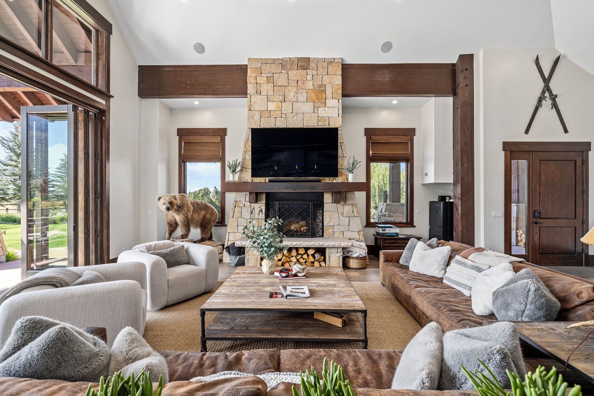 Living room with stone fireplace, large screen TV, bear statue, and brown leather couches.