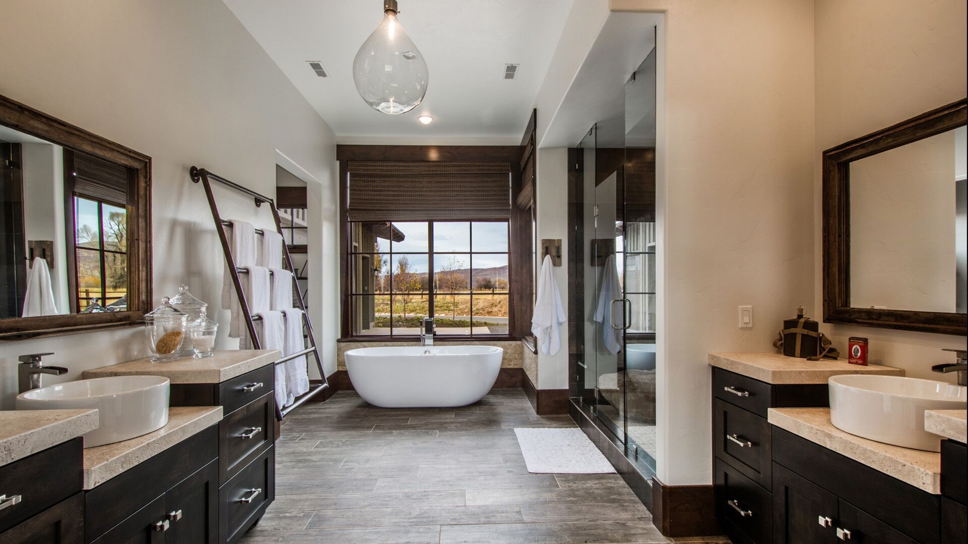 Luxurious bathroom with dark cabinets, double sinks, a freestanding tub, and large windows.