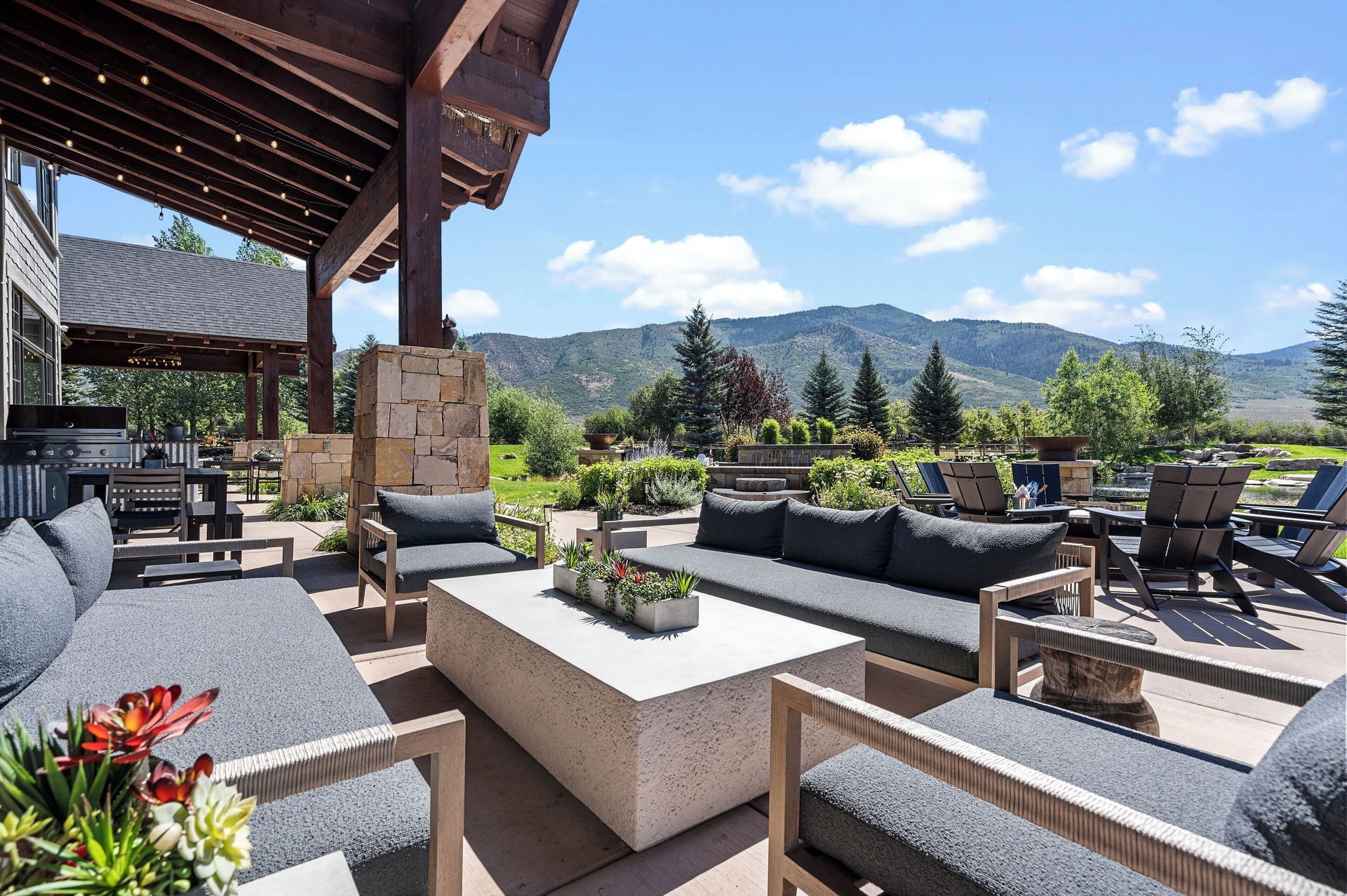 Patio with modern gray furniture, a concrete coffee table, and mountain view under a blue sky.