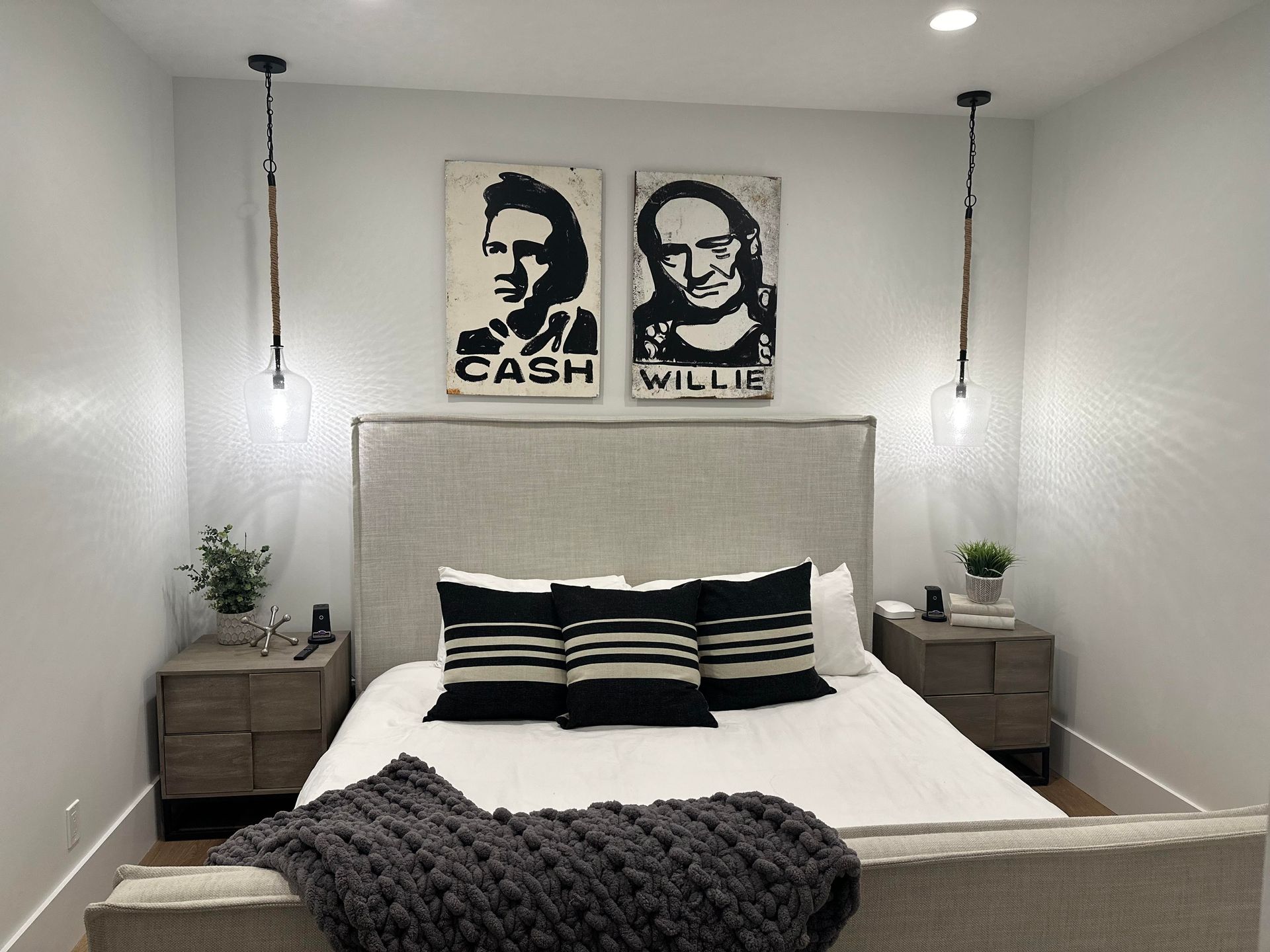 Bedroom with portraits of Johnny Cash and Willie Nelson above the bed, flanked by hanging lights.