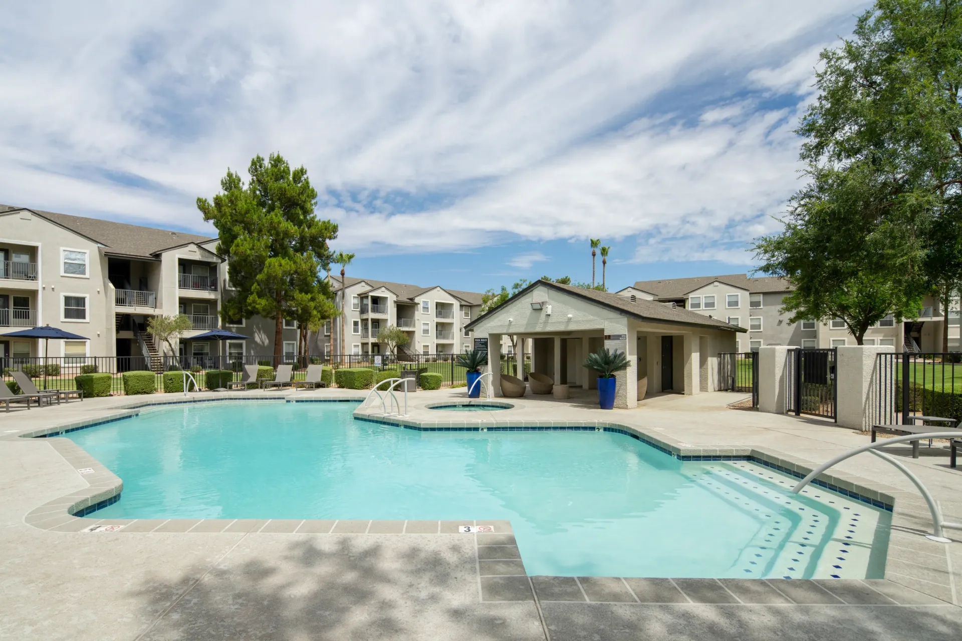 Resort-style swimming pool and spa with lounge chairs and a cabana in a multifamily community.