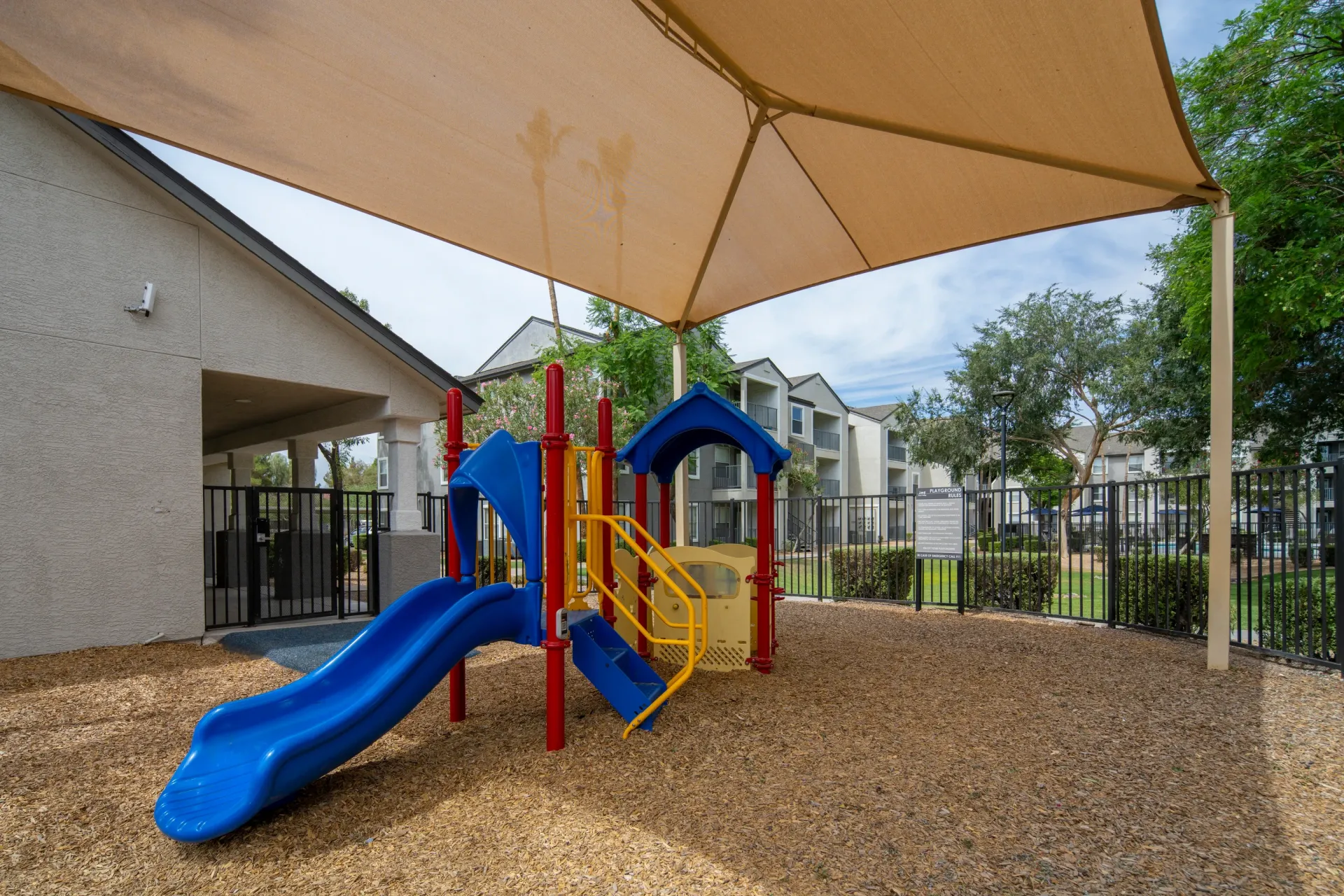Playground with blue slide and yellow accents under a tan shade structure at Heritage at Deer Valley in Phoenix, AZ.