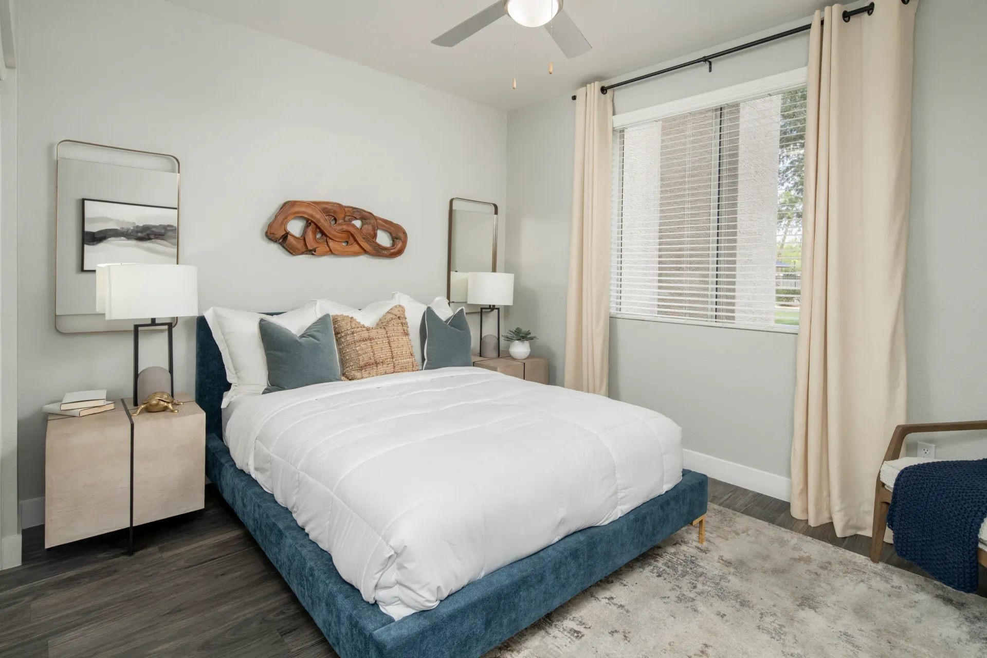 King-size bed with white linens and blue velvet headboard, flanked by nightstands, in a well-lit bedroom at Heritage at Deer Valley in Phoenix, AZ.