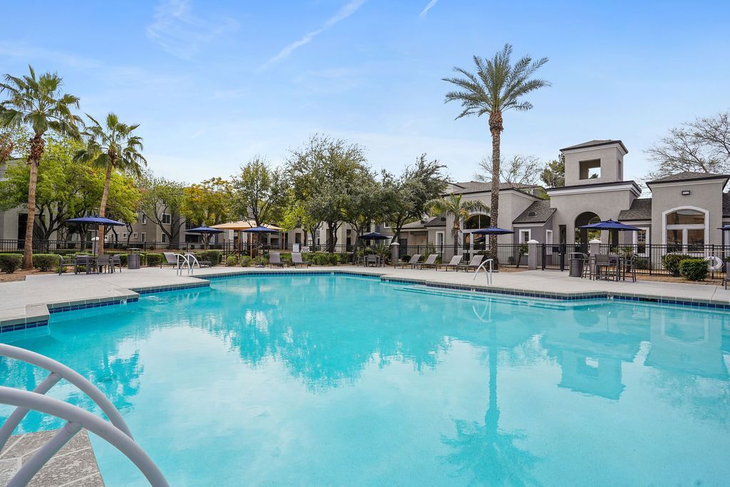 Outdoor apartment community pool with lounge chairs and umbrellas at Heritage at Deer Valley in Phoenix, AZ.