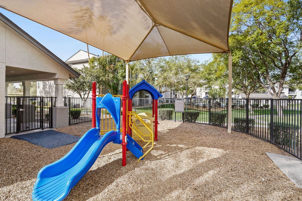 Playground with a blue slide and colorful climbing structure under a shade sail in a gated apartment community at Heritage at Deer Valley in Phoenix, AZ.