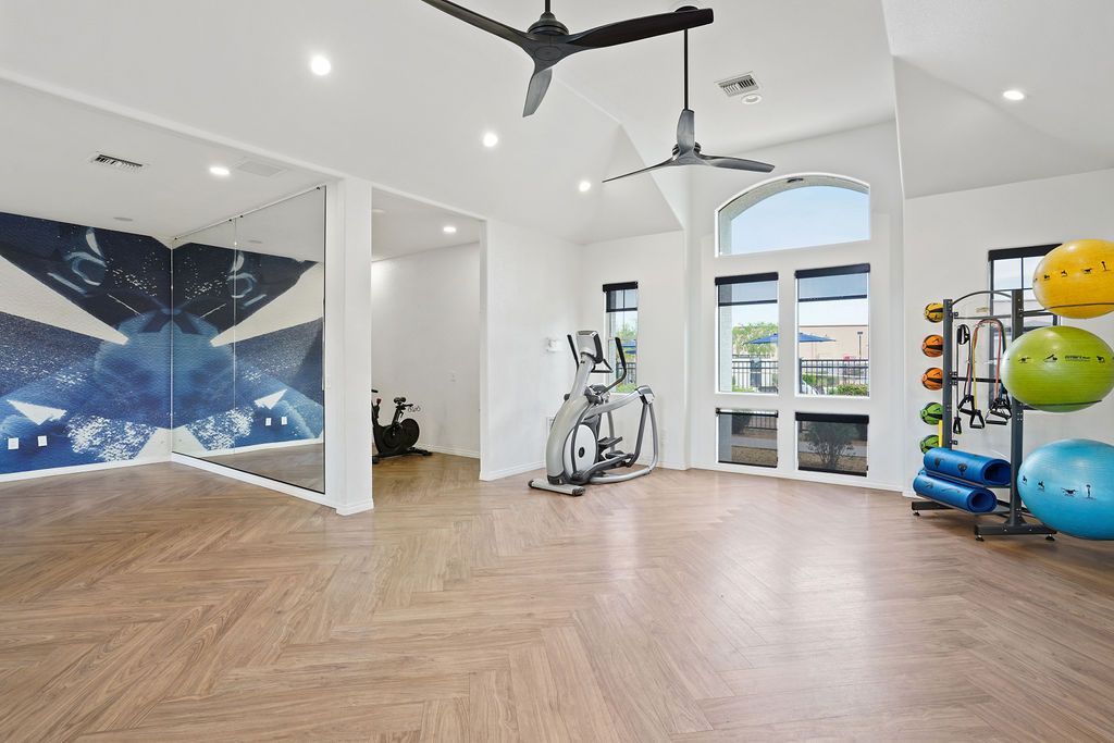 Interior community gym with treadmill, stationary bike, weight rack, mirrors, and large windows at Heritage at Deer Valley in Phoenix, AZ.