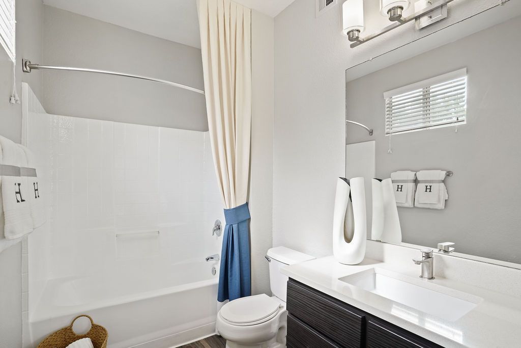 Bathroom with white sink and vanity, mirror, toilet, and a bathtub with a shower curtain at Heritage at Deer Valley in Phoenix, AZ.