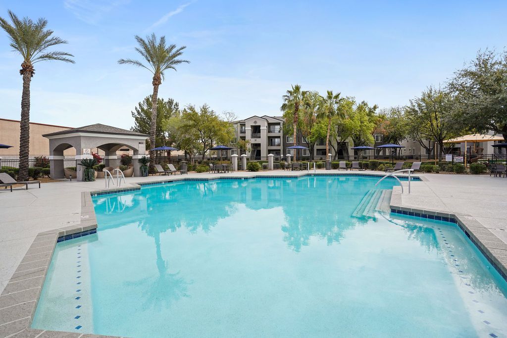 Outdoor pool at a multifamily community with palm trees, lounge chairs, and umbrellas at Heritage at Deer Valley in Phoenix, AZ.