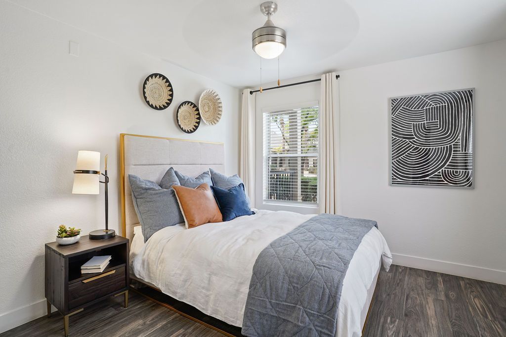 Bedroom with a large bed, nightstand, window, and abstract wall art at Heritage at Deer Valley in Phoenix, AZ.