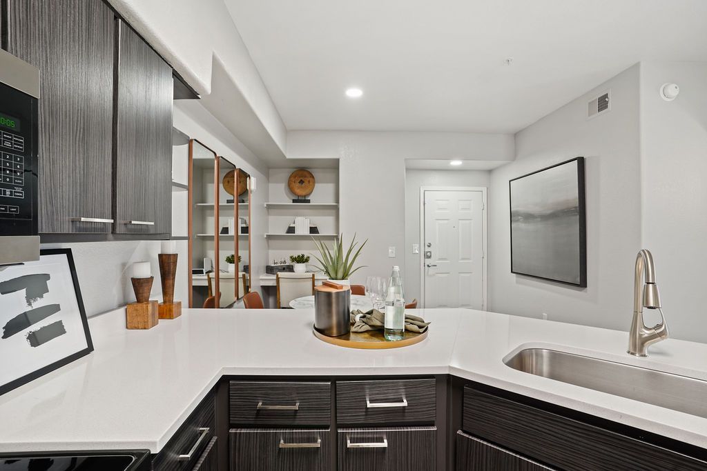 Open kitchen with white countertops, dark wood cabinets, and a stainless steel sink at Heritage at Deer Valley in Phoenix, AZ.
