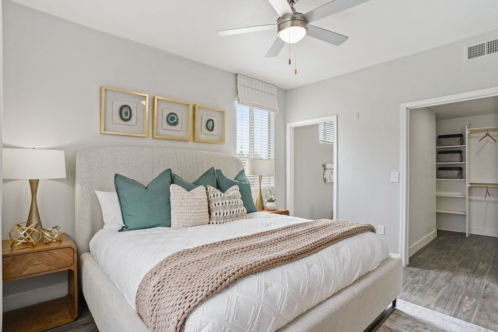 Bedroom in an apartment with padded headboard bed, nightstands, ceiling fan, and open closet at Heritage at Deer Valley in Phoenix, AZ.