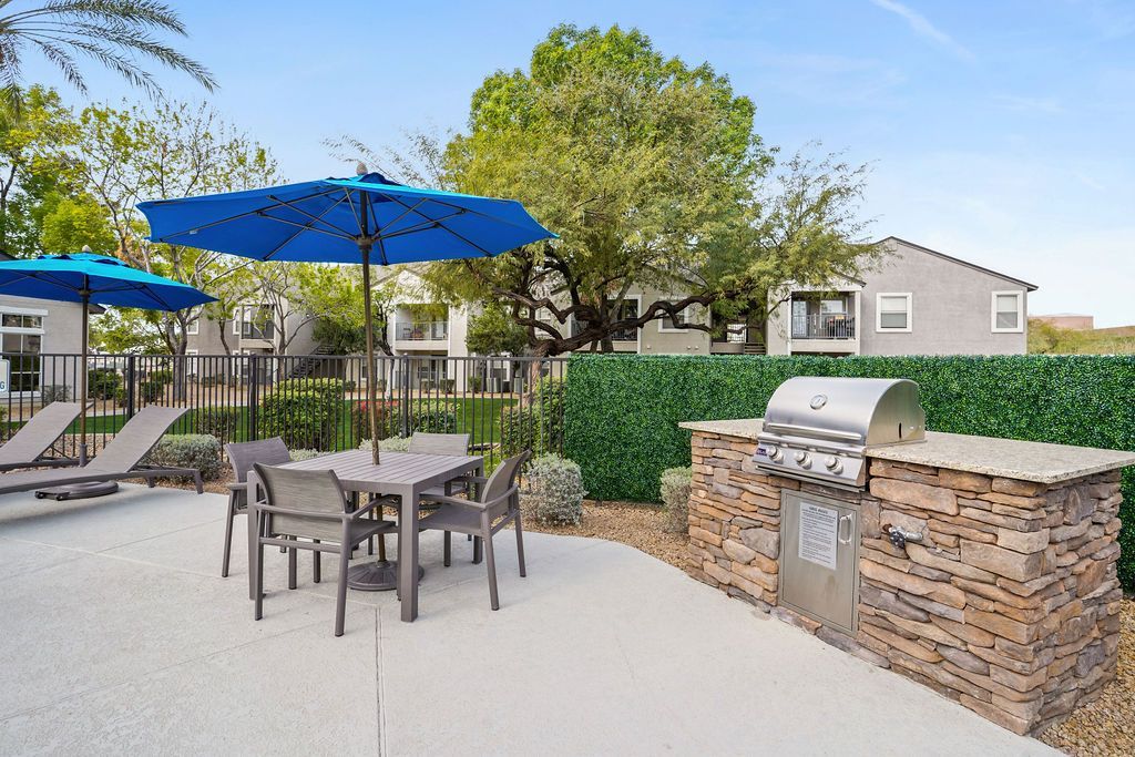 Outdoor communal grilling area with table, chairs, and blue umbrellas at Heritage at Deer Valley in Phoenix, AZ.