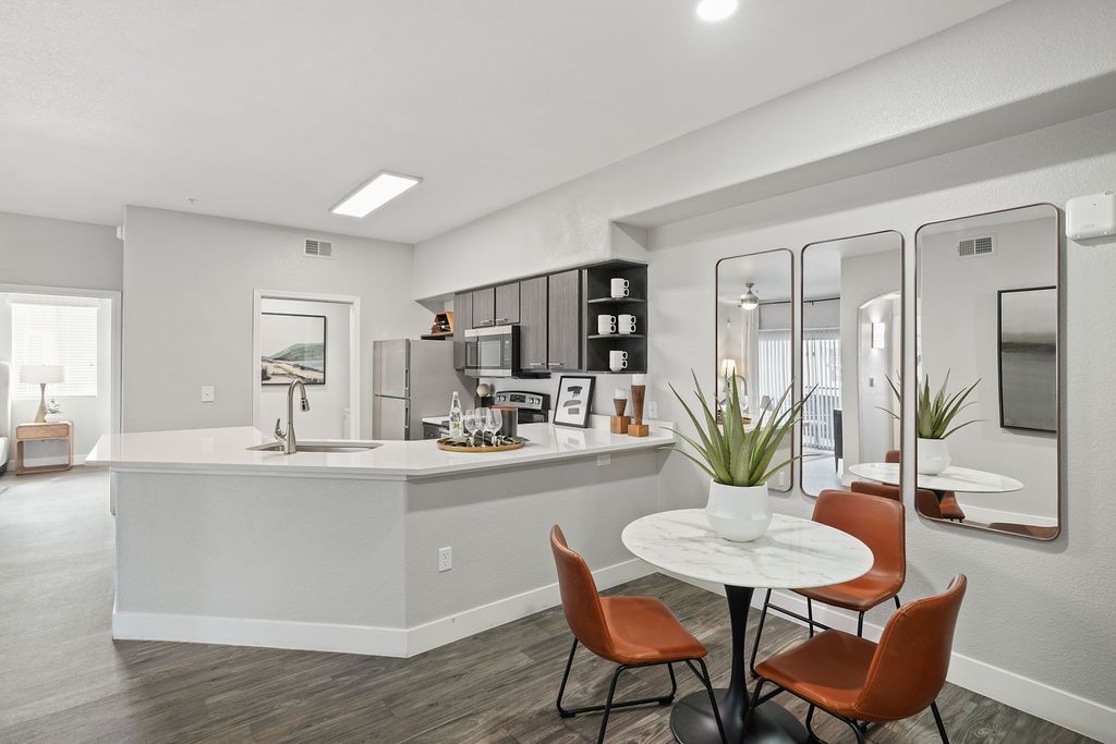 Modern apartment kitchen with white island, stainless appliances, round marble dining table, and orange chairs at Heritage at Deer Valley in Phoenix, AZ.