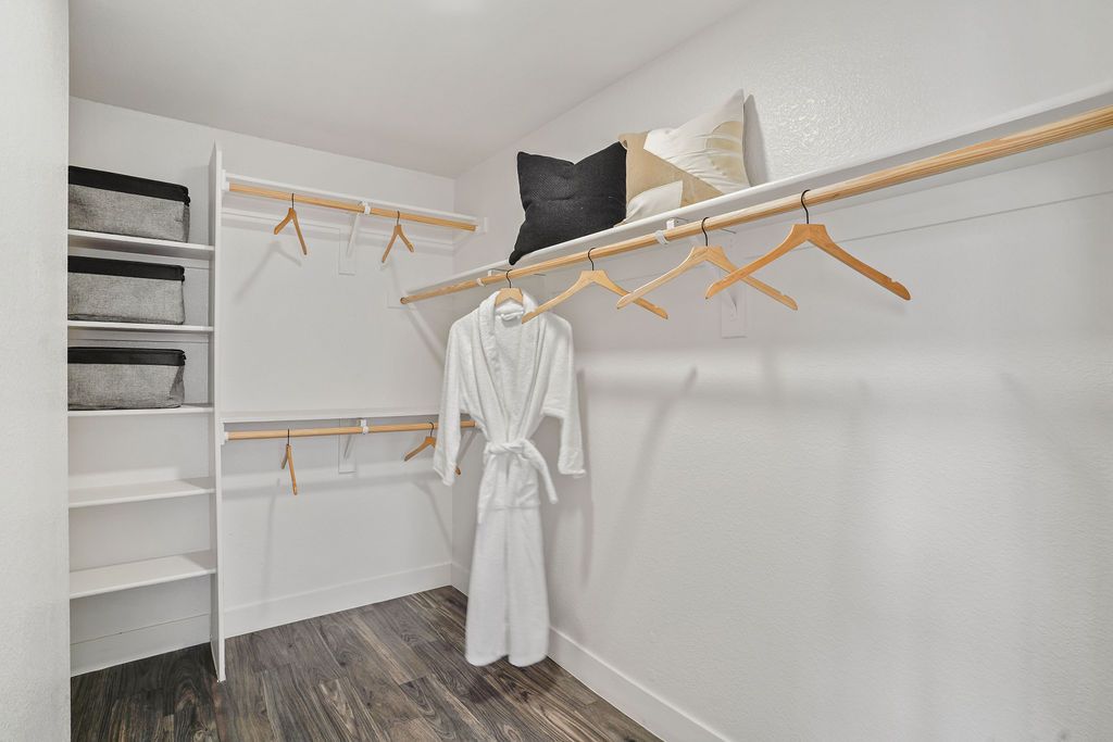 Walk-in closet with white walls, wooden shelves, and two long hanging rods at Heritage at Deer Valley in Phoenix, AZ.