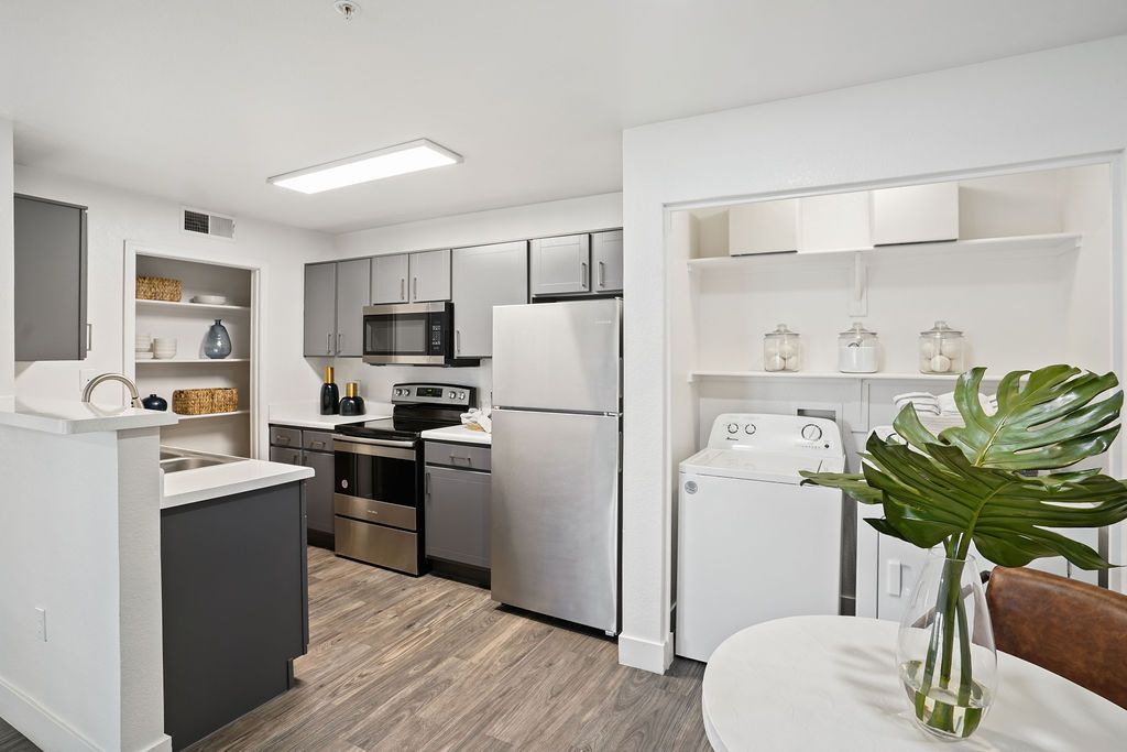 Modern apartment kitchen with gray cabinets, stainless steel fridge, stove, microwave, and a laundry alcove at Heritage at Deer Valley in Phoenix, AZ.