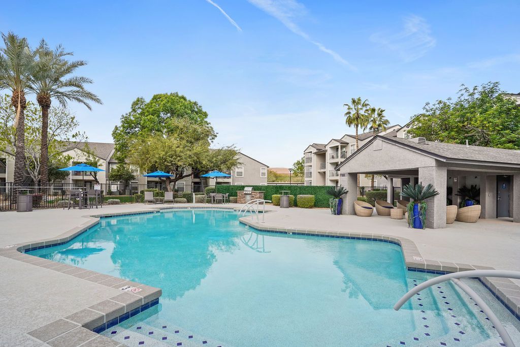 Outdoor apartment pool with lounge chairs, blue umbrellas, and palm trees at Heritage at Deer Valley in Phoenix, AZ.