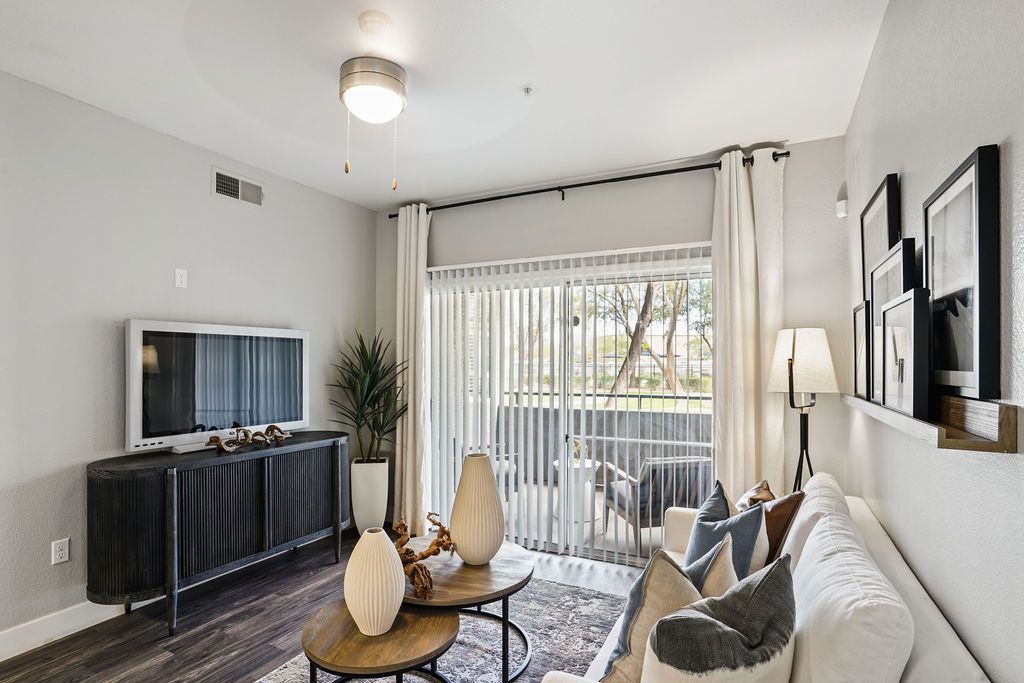 Living room in a modern apartment with a sofa, TV, and sliding glass door to a balcony at Heritage at Deer Valley in Phoenix, AZ.