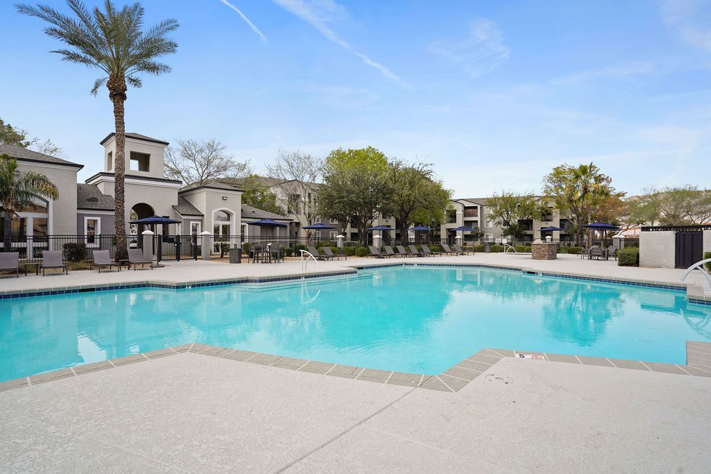 Outdoor apartment community pool with lounge chairs, umbrellas, and palm trees at Heritage at Deer Valley in Phoenix, AZ.