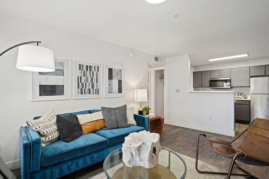 Living room in an apartment with a blue sofa, abstract wall art, and an open kitchen at Heritage at Deer Valley in Phoenix, AZ.