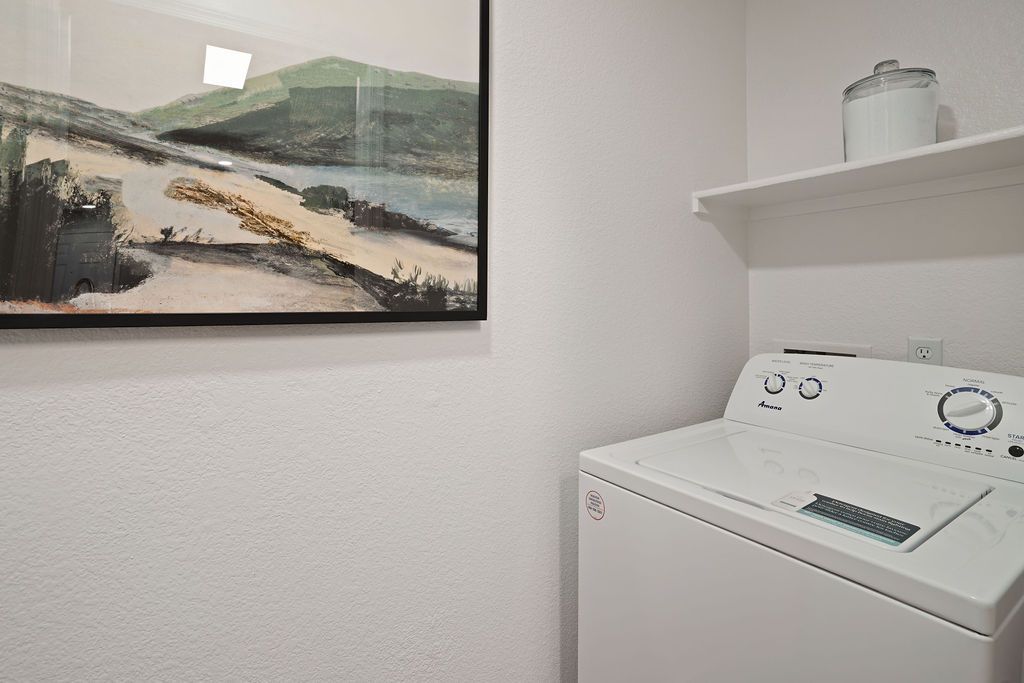 White top-load washing machine in a small laundry closet with a shelf at Heritage at Deer Valley in Phoenix, AZ.