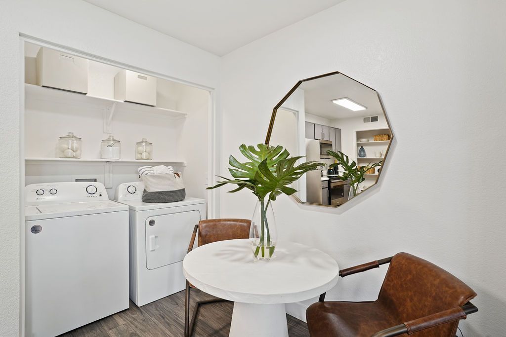 Laundry closet in an apartment with a washer and dryer, shelves, and a small round table with two chairs at Heritage at Deer Valley in Phoenix, AZ.