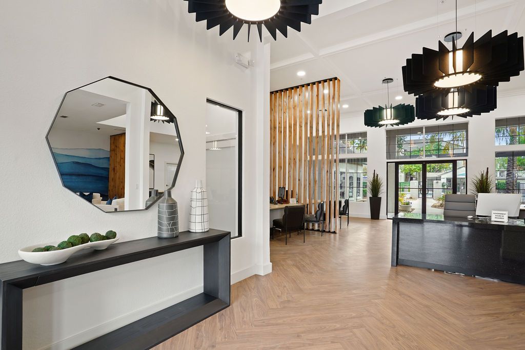 Modern apartment lobby with reception desk, large mirror, and pendant lights at Heritage at Deer Valley in Phoenix, AZ.